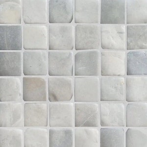 May include: A close-up of a wall tiled with small, square, light gray stone tiles. The tiles have a slightly irregular shape and a subtle, textured surface.
