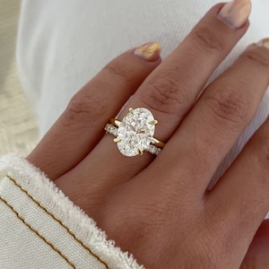 May include: A close-up of a hand wearing a gold band with a large oval-shaped diamond ring and a smaller diamond band.