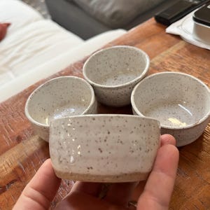 Op de afbeelding: Vier kleine, gespikkelde keramische kommen. De kommen zijn gebroken wit met donkerbruine spikkels en een natuurlijke, ongeglazuurde basis. De kommen zijn rond met een licht schuine rand, perfect voor het serveren van dips of kleine porties.