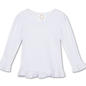 Puede incluir: Camiseta blanca de manga larga con dobladillo y pu&ntilde;os con volantes. La camiseta tiene un cuello redondo.