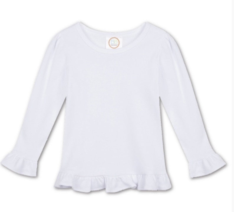 Puede incluir: Camiseta blanca de manga larga con dobladillo y pu&ntilde;os con volantes. La camiseta tiene un cuello redondo.