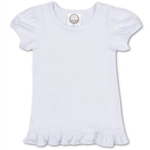 Puede incluir: Camiseta blanca de manga corta con un dobladillo con volantes. La camiseta tiene un escote redondo y una peque&ntilde;a etiqueta con las letras "BB" en la parte delantera.