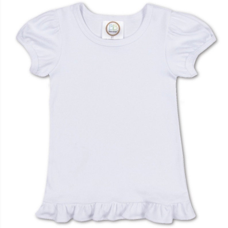 Puede incluir: Camiseta blanca de manga corta con un dobladillo con volantes. La camiseta tiene un escote redondo y una peque&ntilde;a etiqueta con las letras "BB" en la parte delantera.