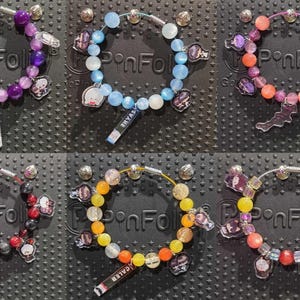 May include: Six beaded bracelets featuring various colored spheres, including purple, light blue, orange, red, yellow, and multicolored beads. Each bracelet includes small character charms and a rectangular tag with printed text.