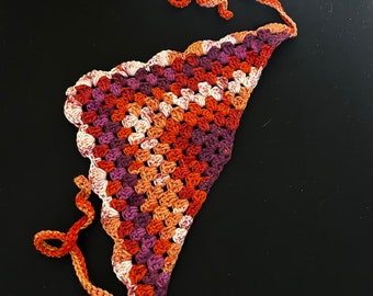 May include: A crocheted triangle scarf with a scalloped edge in shades of orange, brown, and purple. The scarf has two long ties.