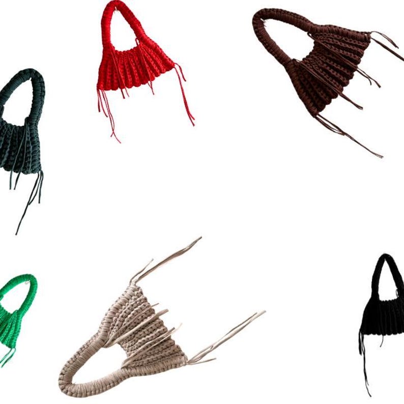May include: A collection of handmade crochet bags in various colors, including red, black, brown, green, and beige. Each bag features a unique design with a handle and fringe details, showcasing a modern, artistic aesthetic.