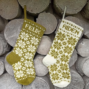 May include: Two knit Christmas stockings featuring a fair isle snowflake pattern in olive green and cream. The left stocking is primarily olive green with the name FELIX in cream, while the right stocking is primarily cream with the name AIDEN in olive green.