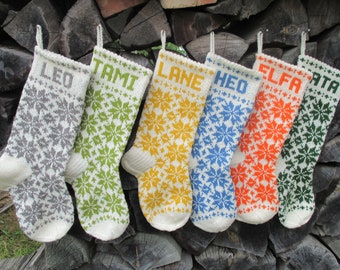 May include: Six hand-knitted Christmas stockings featuring a white base with colorful snowflake patterns and personalized names at the top. The names LEO, TAMI, LANE, HEO, ELFA, and ATA are knitted in grey, green, yellow, blue, orange, and dark green.