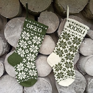 May include: Two knit Christmas stockings featuring a repeating snowflake pattern. The left stocking is dark green with white details and the name GREG. The right stocking is white with dark green details and the name JOOSU. Both have hanging loops.