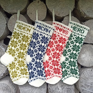 May include: Four knitted Christmas stockings featuring a white base with intricate snowflake patterns in olive green, navy blue, red, and dark green. Each stocking is personalized with the names AIDEN, MICAH, ANAIS, and HERO in block letters.