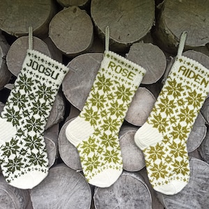 May include: Three knitted Christmas stockings featuring a white and green snowflake pattern. Each stocking has a hanging loop and is personalized with the names JOOSU, ROSE, and AIDEN in green block letters at the top of the cuff.