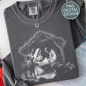 May include: Dark gray long-sleeve shirt with a graphic of the Nativity scene. The image depicts Mary, Joseph, and baby Jesus in a manger, with an animal. A silver necklace with a sun pendant is on the shirt. The text "PNG DIGITAL DESIGN" is on the shirt.