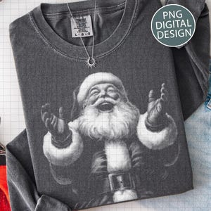 May include: Dark gray long-sleeve shirt featuring a black and white graphic of Santa Claus with his arms raised and mouth open. The shirt has a crew neck and a tag that reads "COMFORT COLORS". A silver necklace with a sun pendant is also visible. The words "PNG DIGITAL DESIGN" are in a circle.