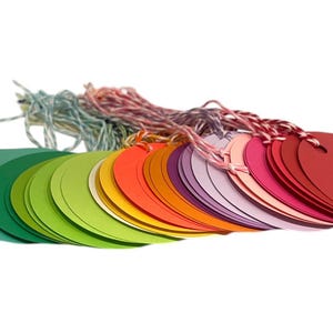 May include: A stack of colourful round paper gift tags with string attached. The tags are arranged in a rainbow pattern, starting with blue and green and ending with red.