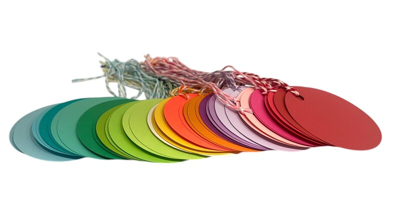May include: A stack of colourful round paper gift tags with string attached. The tags are arranged in a rainbow pattern, starting with blue and green and ending with red.
