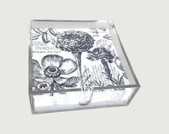 Op de afbeelding: Een heldere acryl tissuebox met een botanische print in zwart en wit. Het heeft bloemenillustraties en tekst. De doos is rechthoekig met een gleuf voor het afgeven van tissues.