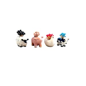 Puede incluir: Cuatro porta-palillos de dientes de cerámica con forma de animales. Una oveja blanca, un cerdo rosa, una gallina blanca y una vaca negra y blanca. Cada animal tiene palillos de dientes que sobresalen de su cabeza.