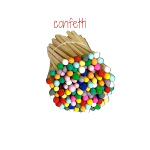 May include: A bundle of wooden matches tied together with a thin string, featuring round tips in a variety of colors including red, blue, green, yellow, pink, and white. The word confetti is printed in red text above the match bundle.