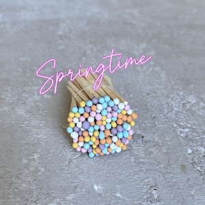 Puede incluir: Un montón de cerillas coloridas con puntas de color azul pastel, rosa, amarillo y naranja. Las cerillas están agrupadas y las puntas están orientadas hacia afuera.