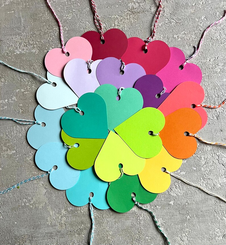 May include: A colourful arrangement of heart-shaped paper tags with string attached. The tags are in various shades of red, pink, purple, blue, green, yellow, and orange.