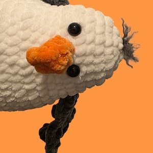 Op de afbeelding: Een zacht, wit zeemeeuw speelgoed met een pluizige textuur, met een feloranje snavel, zwarte ogen en grijze accenten. De tekst "Jellycat inspired" en "Stanley seagull PDF Pattern" zijn zichtbaar.