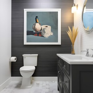 May include: A bathroom scene featuring a framed painting of a duck and a roll of toilet paper. The painting hangs above a white toilet. The room has a dark gray accent wall, a white vanity, and a decorative mirror.