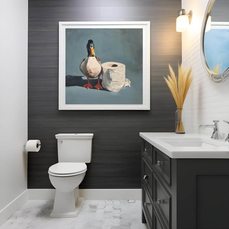 May include: A bathroom scene featuring a framed painting of a duck and a roll of toilet paper. The painting hangs above a white toilet. The room has a dark gray accent wall, a white vanity, and a decorative mirror.