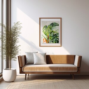 Puede incluir: Un sofá de terciopelo marrón con dos cojines blancos se encuentra frente a una pared blanca con una pintura de acuarela enmarcada de plantas tropicales. La pintura está en un marco de madera claro.