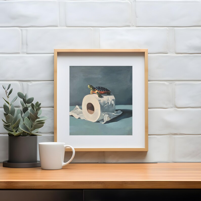 May include: A framed art print featuring a turtle perched atop a roll of toilet paper. The artwork has a blue and white color palette, with a wooden frame. The turtle has a green, red, and black shell.