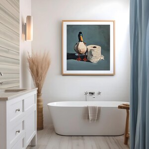 May include: A framed artwork depicts a duck standing next to a roll of toilet paper. The duck has a white body, black head, and orange beak and feet. The artwork is in a bathroom setting with a white bathtub and blue curtain.
