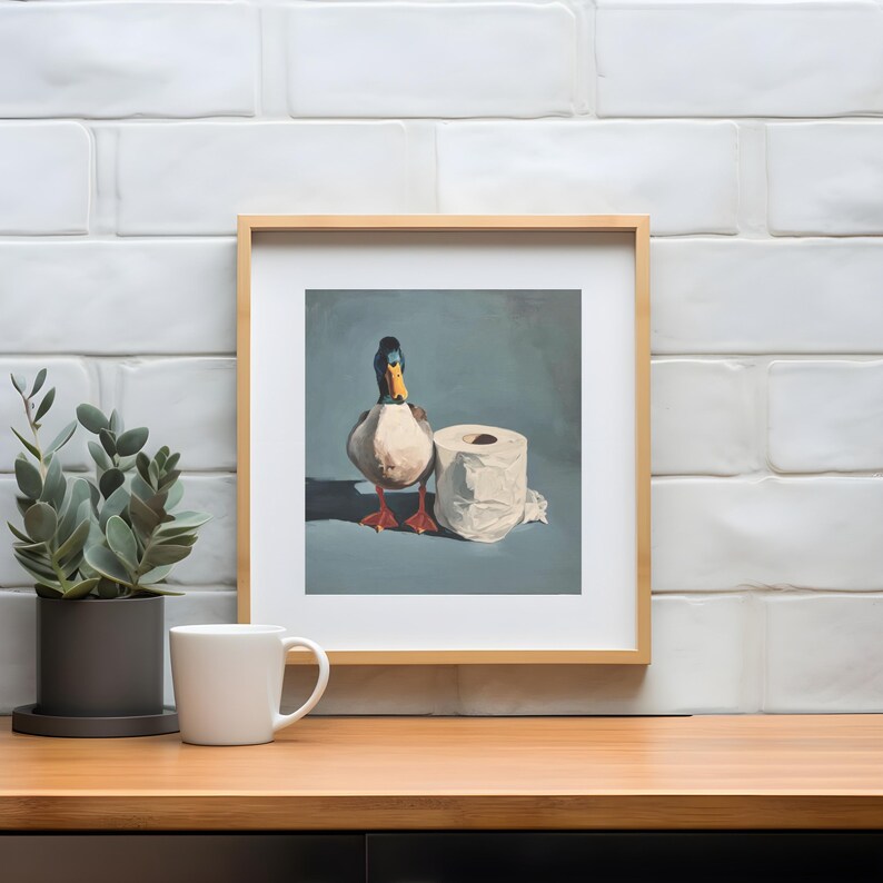 May include: Framed artwork featuring a duck standing next to a roll of toilet paper. The duck has a white body, a blue and black head, and orange feet. The background is a muted blue.