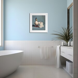 May include: A framed artwork depicts a mallard duck standing next to a roll of toilet paper. The duck has a green head, white neck ring, and brown body. The artwork is set against a blue background, creating a humorous bathroom-themed piece.