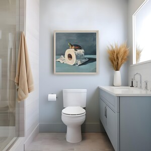 May include: A framed painting depicts a turtle atop a roll of toilet paper. The artwork is displayed in a modern bathroom with a white toilet, a light blue vanity, and a shower with a beige towel. The room has a minimalist design.