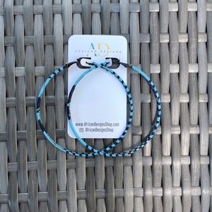 May include: A pair of large hoop earrings made of blue and black fabric with a geometric pattern. The earrings are displayed on a white card with the text "African Designs" and the website address "www.AfricanDesignsShop.com".