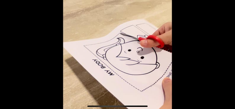 Puede incluir: Una actividad de manualidades imprimible en blanco y negro para ni&ntilde;os. La imprimible presenta un personaje de dibujos animados con el texto "MY BODY" en la p&aacute;gina. Un par de tijeras rojas est&aacute; recortando el personaje.