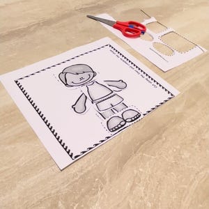 Puede incluir: Una actividad de manualidades de papel imprimible en blanco y negro con una figura de ni&ntilde;o con un borde punteado. La figura del ni&ntilde;o est&aacute; recortada y lista para ser ensamblada.