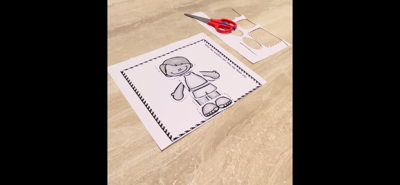Puede incluir: Una actividad de manualidades de papel imprimible en blanco y negro con una figura de ni&ntilde;o con un borde punteado. La figura del ni&ntilde;o est&aacute; recortada y lista para ser ensamblada.