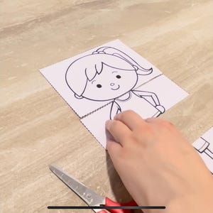 Puede incluir: Un dibujo en blanco y negro de una ni&ntilde;a con una coleta, que lleva una camisa, en una hoja de papel blanca. Una mano sostiene el papel y un par de tijeras rojas est&aacute;n en el fondo.