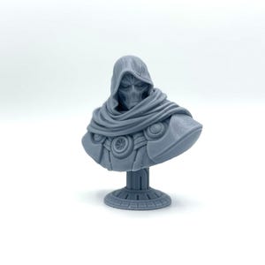May include: A gray 3D printed bust of a hooded figure with a detailed face and intricate armor. The bust is mounted on a round base.