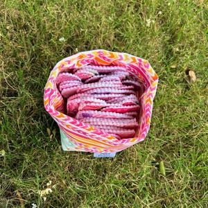 May include: A fabric drawstring bag featuring a vibrant orange, pink, and yellow chevron pattern, filled with a stack of small, round, pink and white quilted fabric pads with scalloped edges and visible stitching throughout the surface.