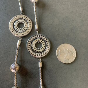 May include: A silver necklace with two large circular pendants and several smaller round beads. The pendants have a concentric circle design with a textured surface.