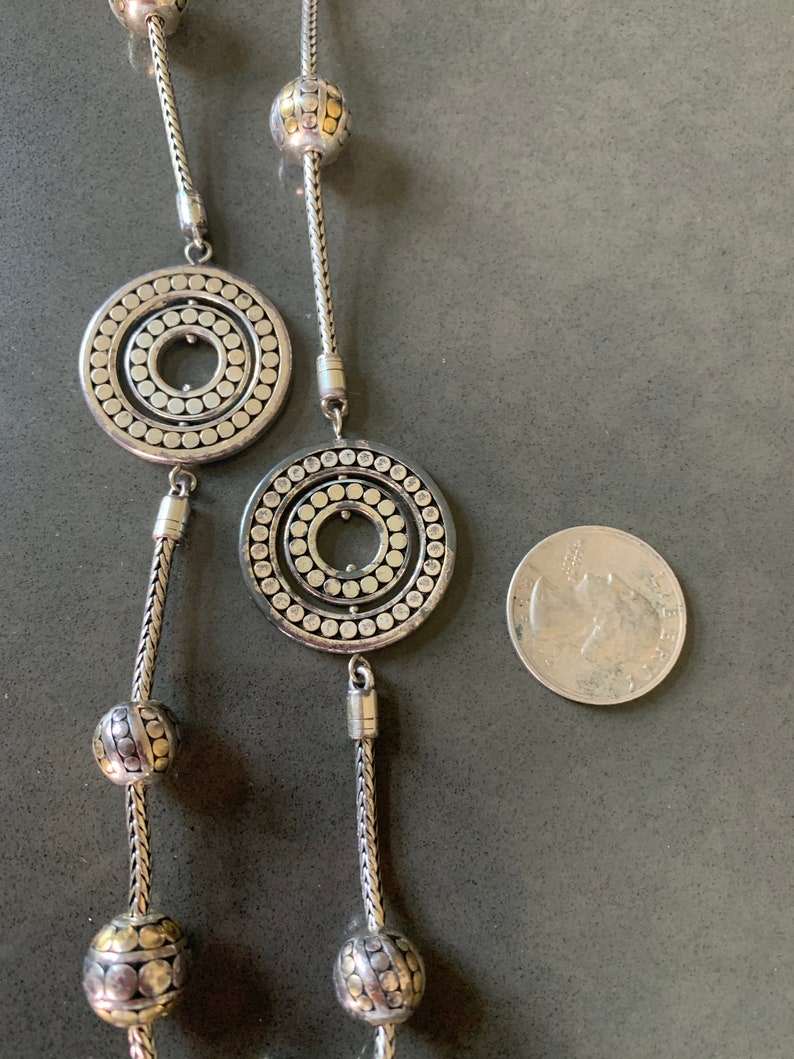 May include: A silver necklace with two large circular pendants and several smaller round beads. The pendants have a concentric circle design with a textured surface.