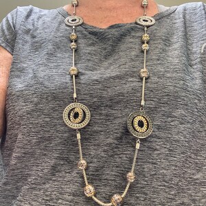 May include: A silver and gold necklace with large circular pendants and smaller round beads.