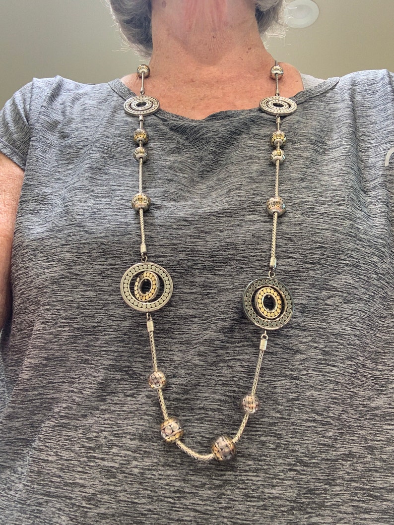 May include: A silver and gold necklace with large circular pendants and smaller round beads.
