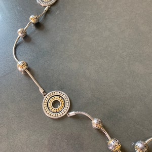 May include: A silver and gold necklace with a chain and round pendants. The pendants are textured with small circles and have a gold center.
