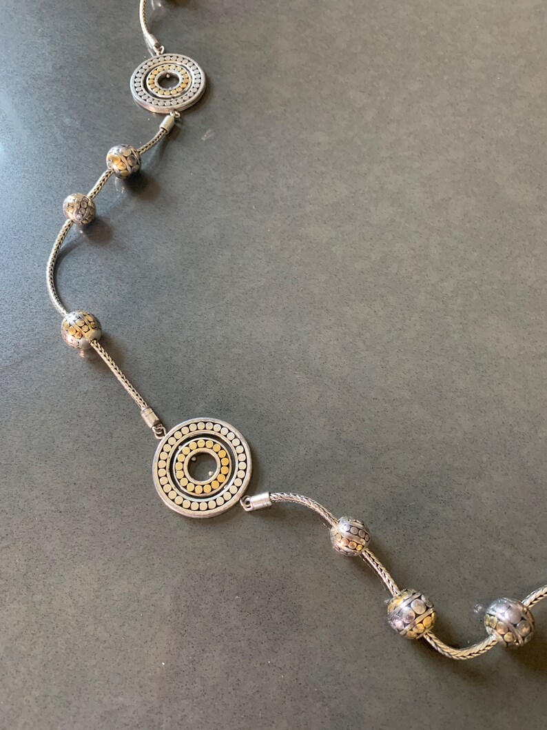 May include: A silver and gold necklace with a chain and round pendants. The pendants are textured with small circles and have a gold center.
