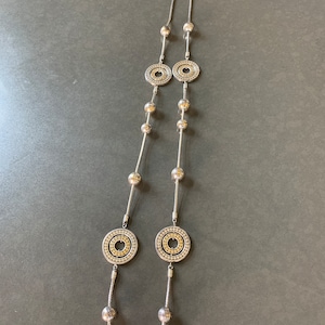 May include: A silver necklace with two large circular pendants and smaller round beads. The pendants have a textured design with a gold center.