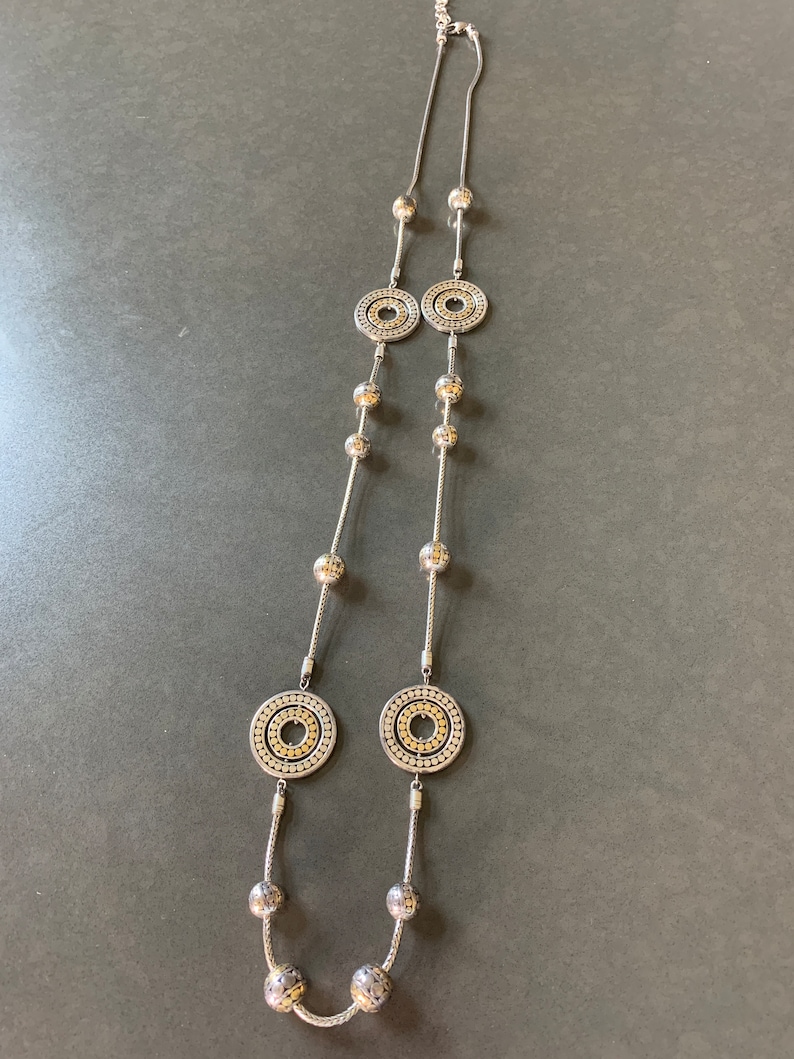 May include: A silver necklace with two large circular pendants and smaller round beads. The pendants have a textured design with a gold center.