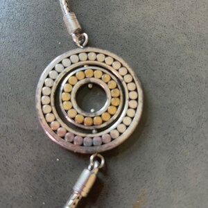May include: A silver chain necklace with a circular pendant. The pendant has a concentric circle design with a gold center.