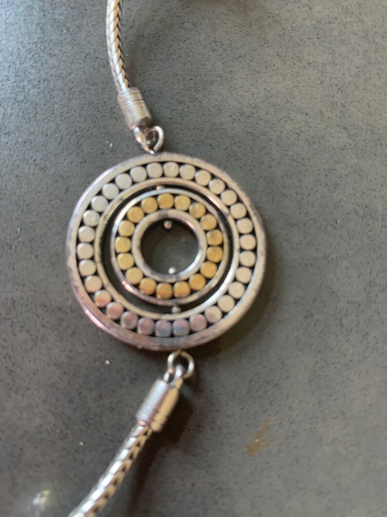 May include: A silver chain necklace with a circular pendant. The pendant has a concentric circle design with a gold center.